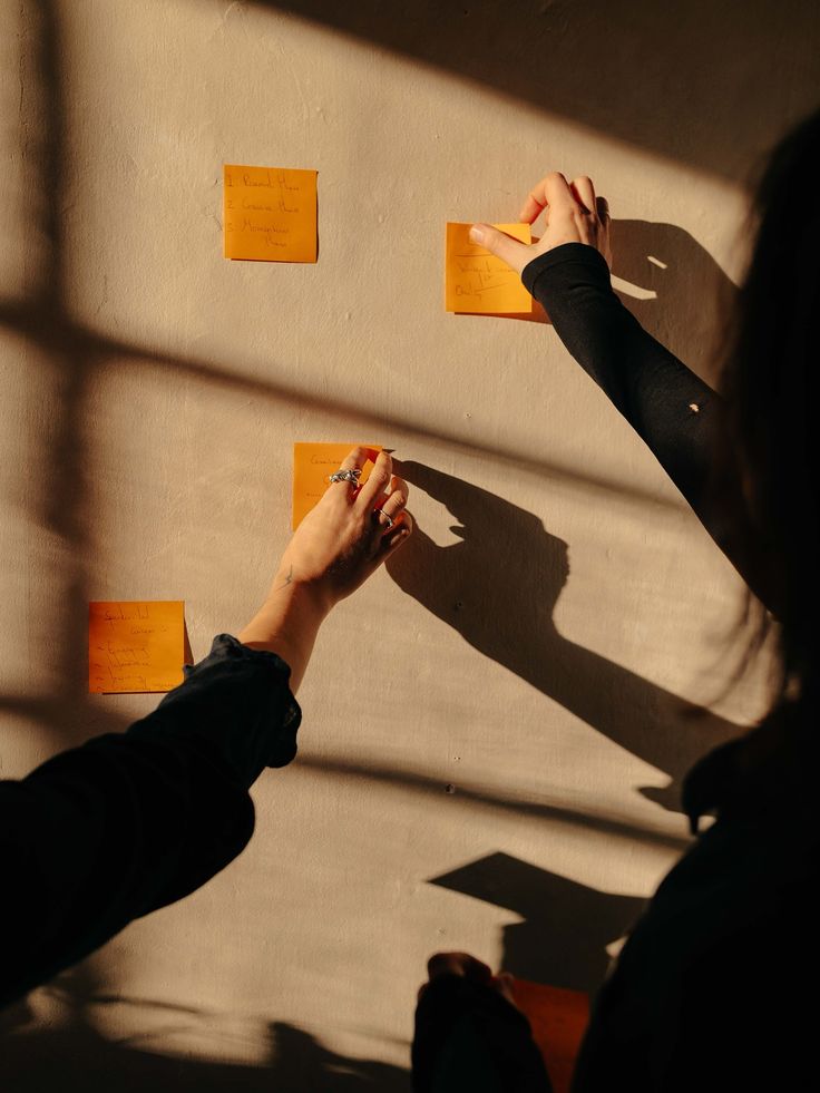 Two hands arranging handwritten notes on a sunlit wall
